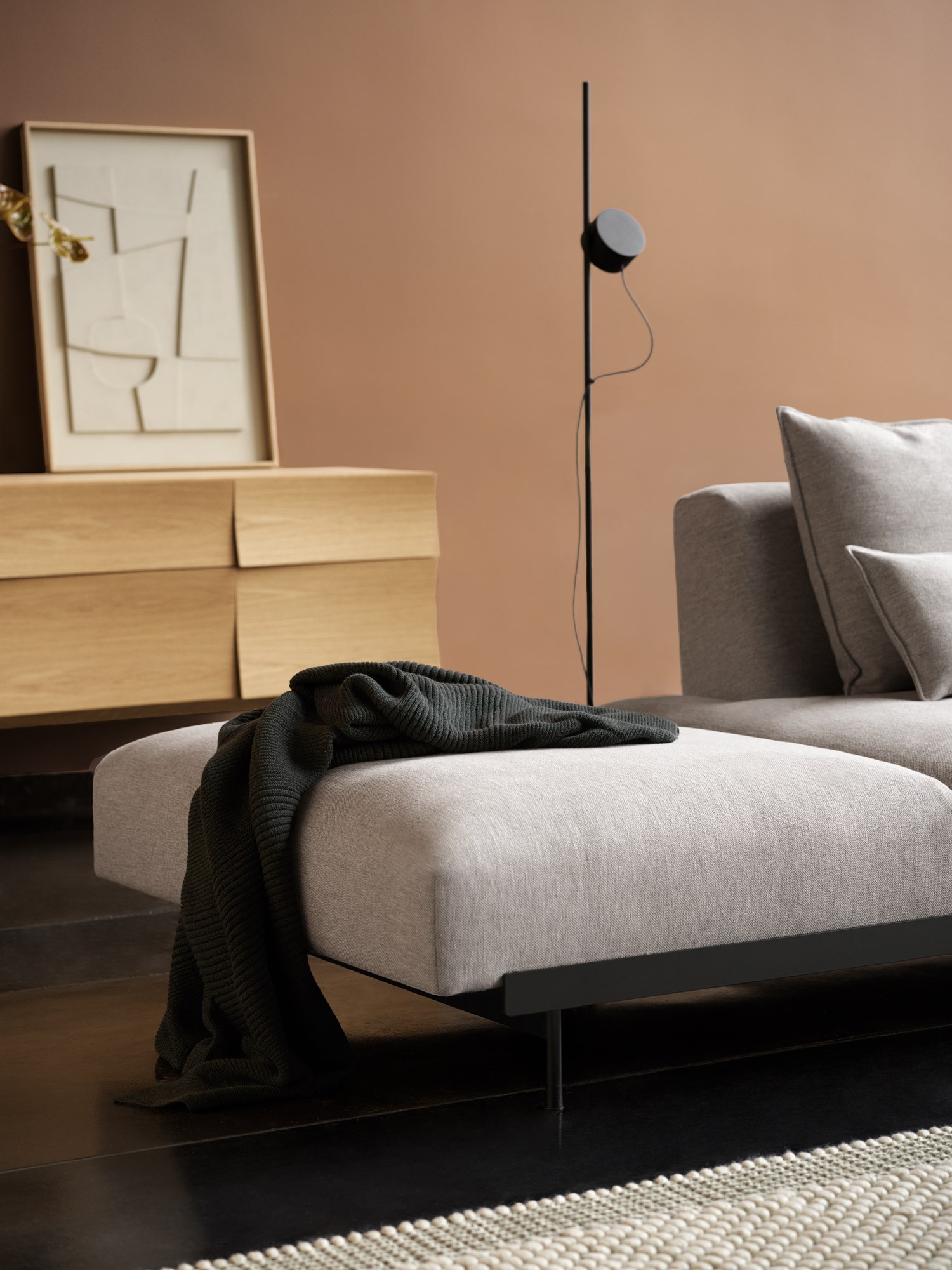 A calm living space with the In Situ Sofa in Clay 12, contrasted by a dark green Rhythm Cushion, light grey Pebble Rug, oak Reflect Sideboard, and Post Floor Lamp. A calm living space with the In Situ Sofa in Clay 12, contrasted by a dark green Rhythm Cushion, light grey Pebble Rug, oak Reflect Sideboard, and Post Floor Lamp.