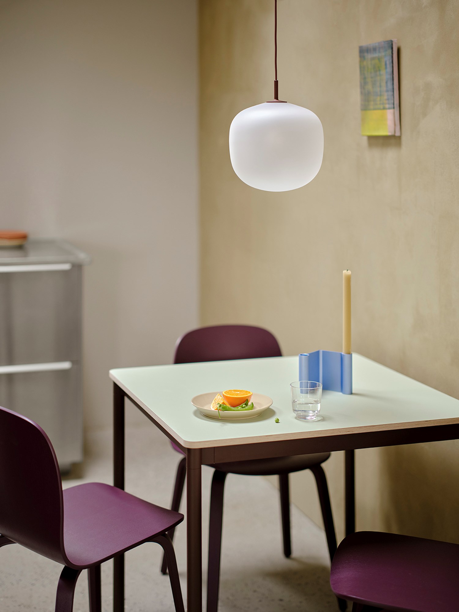 A square base table with a light green, brown, and red color palette, paired with two Visu chairs in dark plum. A light blue Rime Raise accessory is included. A square base table with a light green, brown, and red color palette, paired with two Visu chairs in dark plum. A light blue Rime Raise accessory is included.