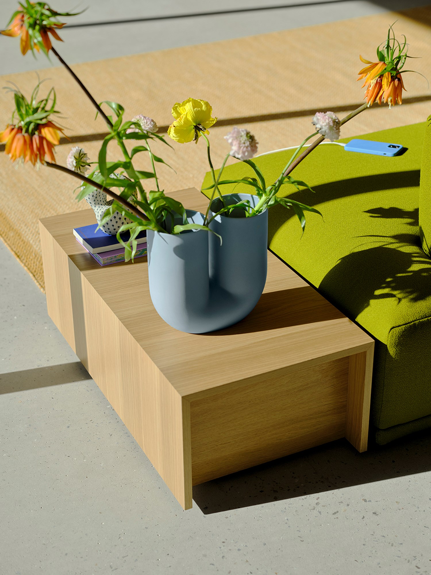 A Connect table in Oak Veneer placed in the sunlight and styled with a Kink Vase in light blue with orange and yellow flowers. A Connect table in Oak Veneer placed in the sunlight and styled with a Kink Vase in light blue with orange and yellow flowers.