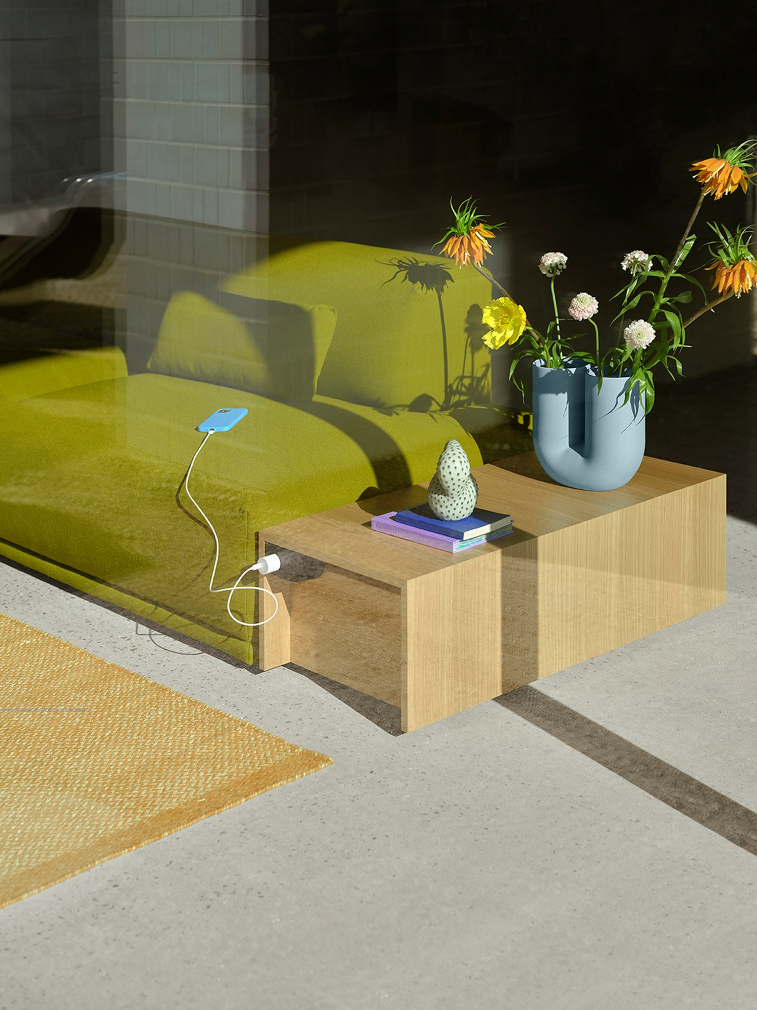 A Connect table in Oak Veneer and Connect Sofa placed in the sunlight and styled with a Kink Vase in light blue with orange and yellow flowers. A Connect table in Oak Veneer and Connect Sofa placed in the sunlight and styled with a Kink Vase in light blue with orange and yellow flowers.