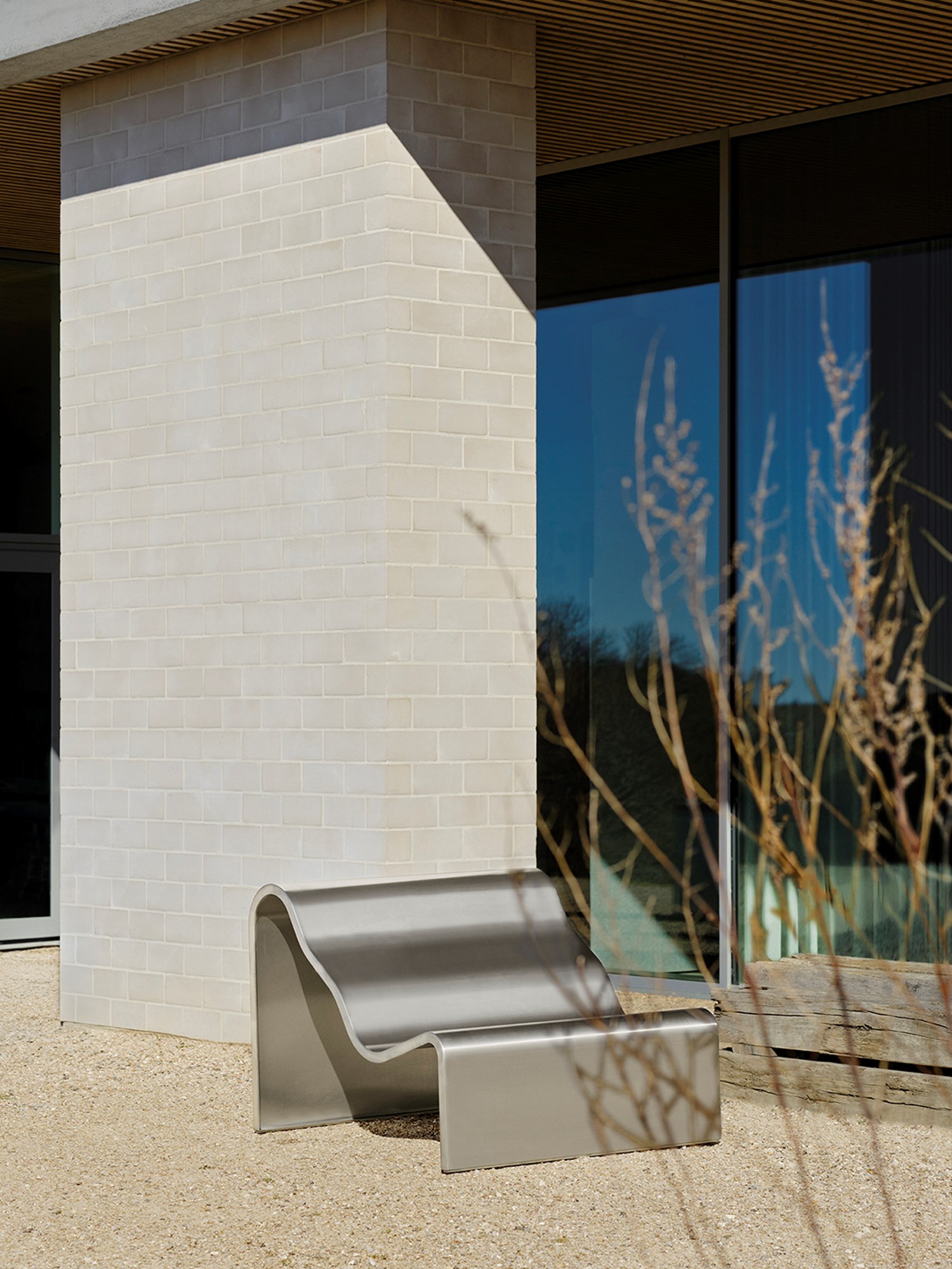 An architectural metal bench with a wavy, sculptural design are placed outside in the sun. An architectural metal bench with a wavy, sculptural design are placed outside in the sun.