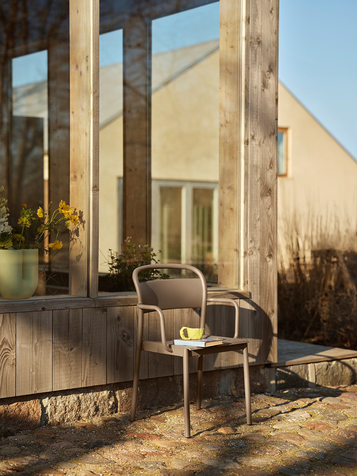 A linear steel armchairin  taupe placed outside in the evening sunlight. A Light green Kink vase in placed behind the chair creating a cozy setting.  A linear steel armchairin  taupe placed outside in the evening sunlight. A Light green Kink vase in placed behind the chair creating a cozy setting.