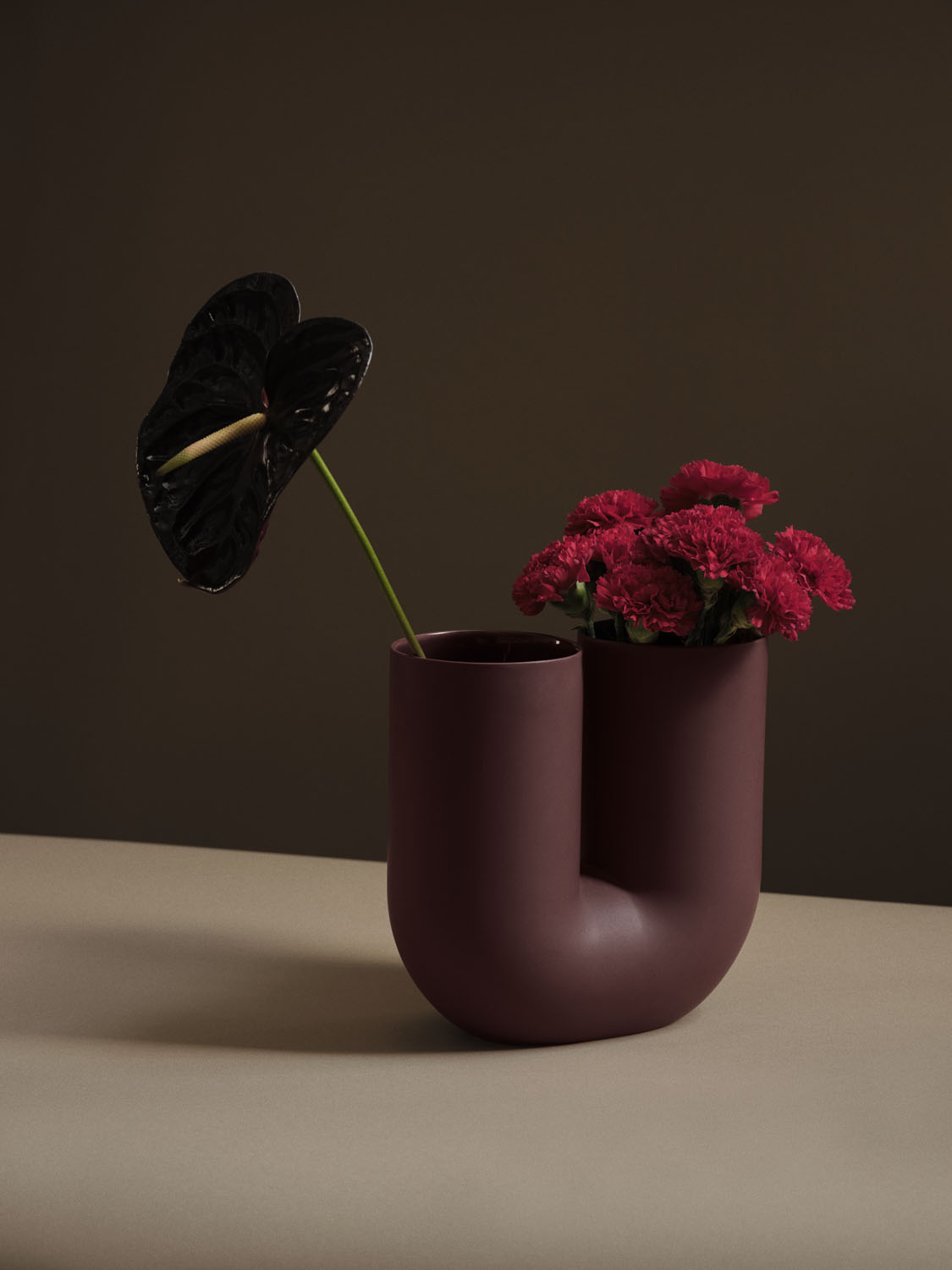 A Muuto Kink vase in deep red, showcasing a sculptural design with smooth, flowing curves. The rich red color and distinctive shape make it a striking decorative piece that adds a touch of  sophistication to any space