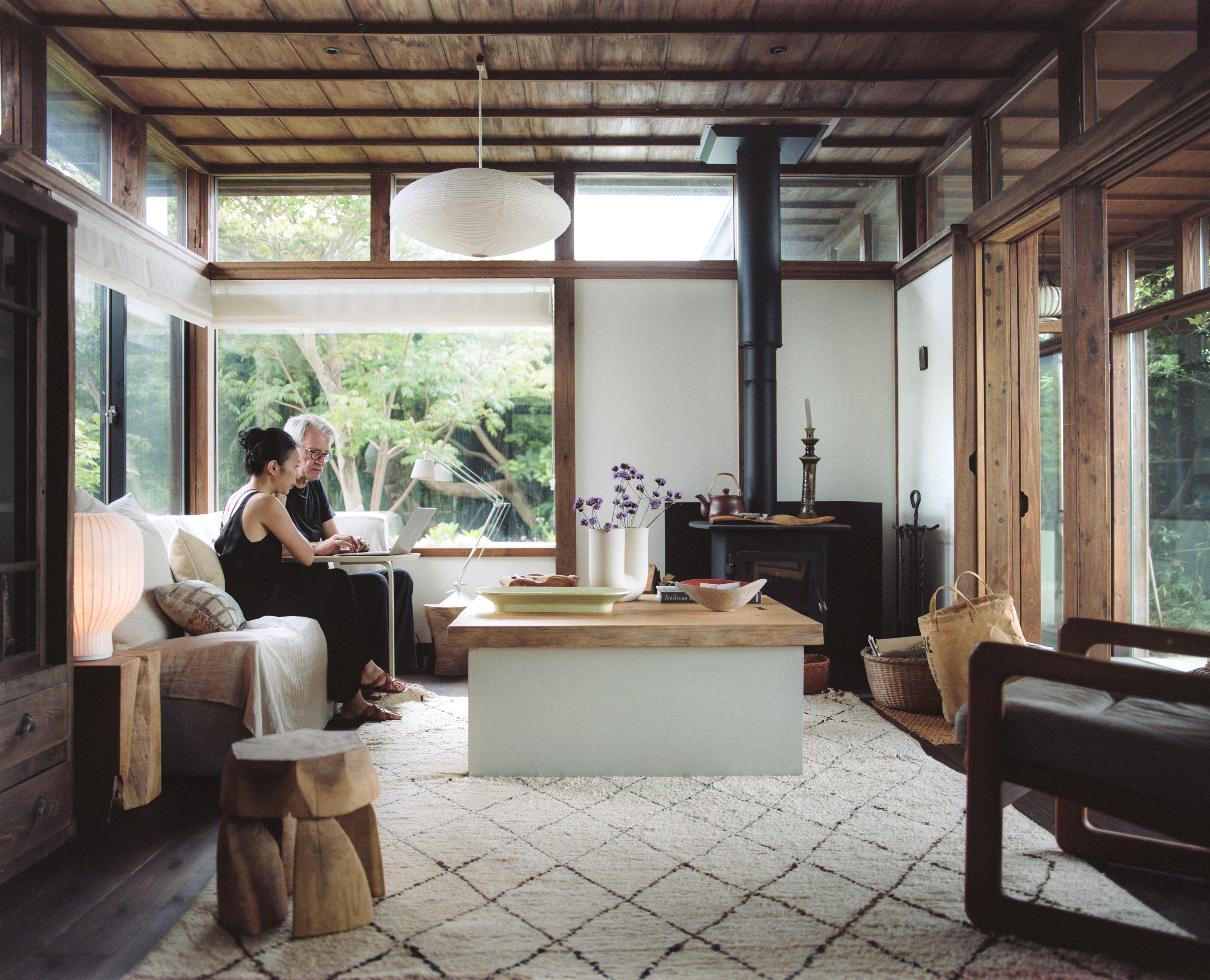 Giselle and Philippe sitting in a wooden Japanese style living room, using a laptop.
