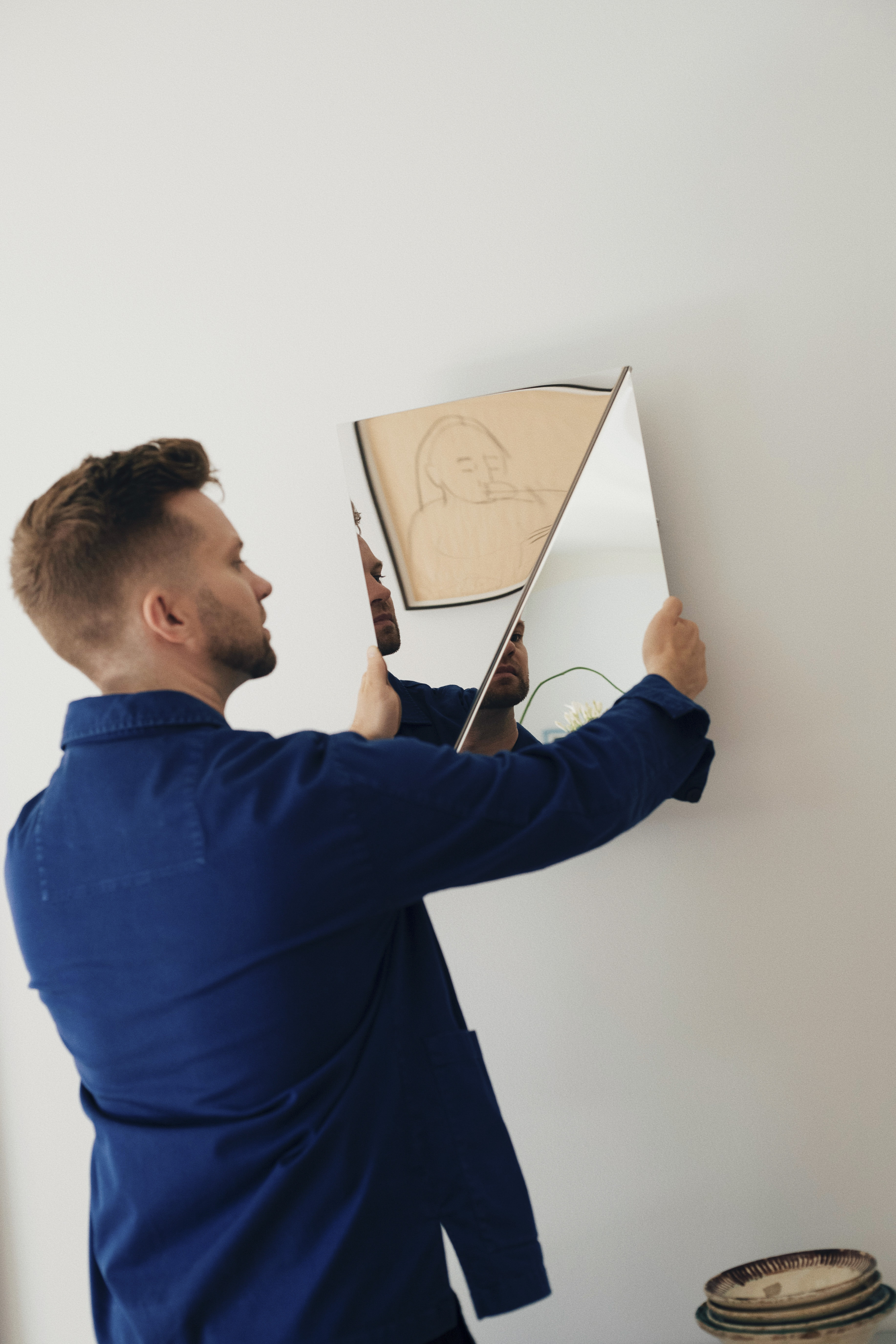 Designer Michael Schneider hanging Gaze Mirror on the wall of his home, captured in a candid moment within a minimal and personal interior.
