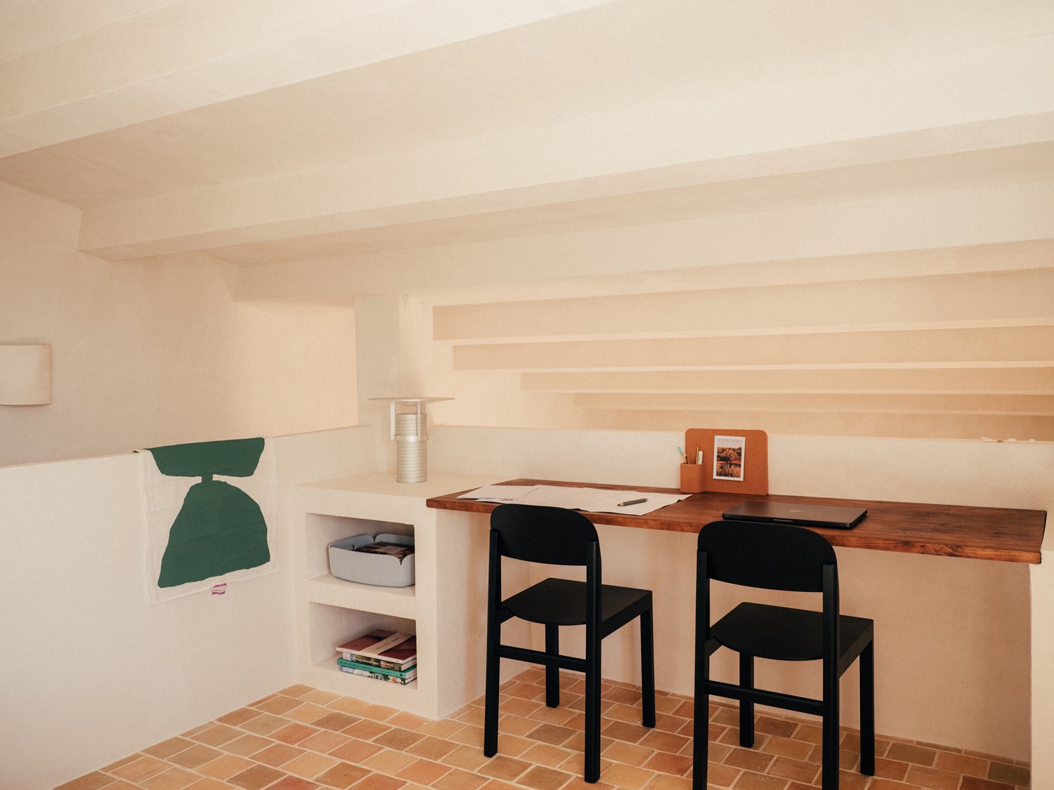 Close-up of a cozy desk setup – A detailed look at a wooden workspace with a sculptural Set Lamp, cork organizer, and a black chair. Below, open built-in shelves store books and a soft gray storage bin, seamlessly blending practicality with the rustic, minimalist decor. Close-up of a cozy desk setup – A detailed look at a wooden workspace with a sculptural Set Lamp, cork organizer, and a black chair. Below, open built-in shelves store books and a soft gray storage bin, seamlessly blending practicality with the rustic, minimalist decor.