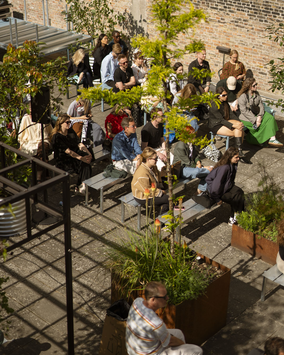 Outdoor courtyard talk hosted by Muuto, featuring speakers and audience seated in a sunlit courtyard with modern Muuto furniture.