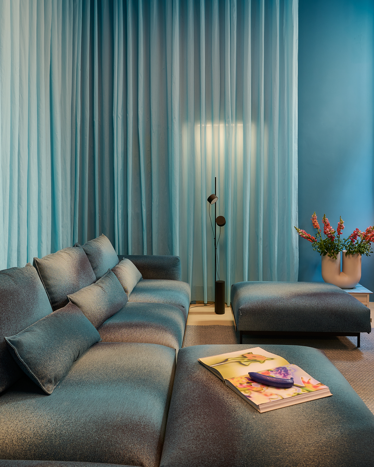 A light blue room with matching curtains. A large dark blue couch is placed along the wall, creating a cozy and comfortable lounge area.