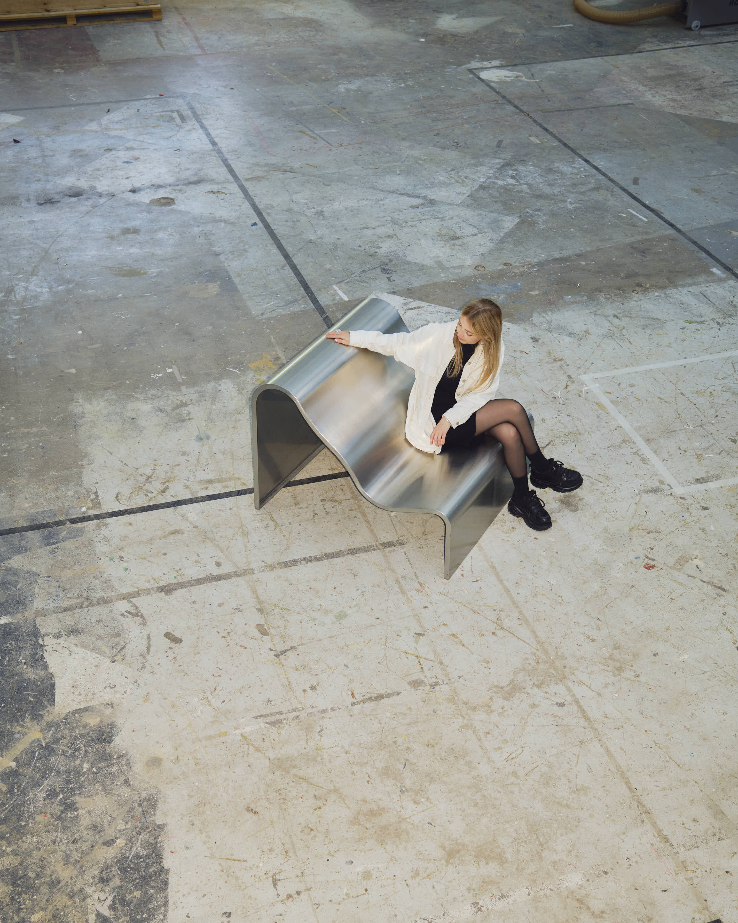 Lise Vester seated on the Dream View Bench in a raw, industrial space, highlighting the contrast between the bench’s soft form and the rough surroundings.