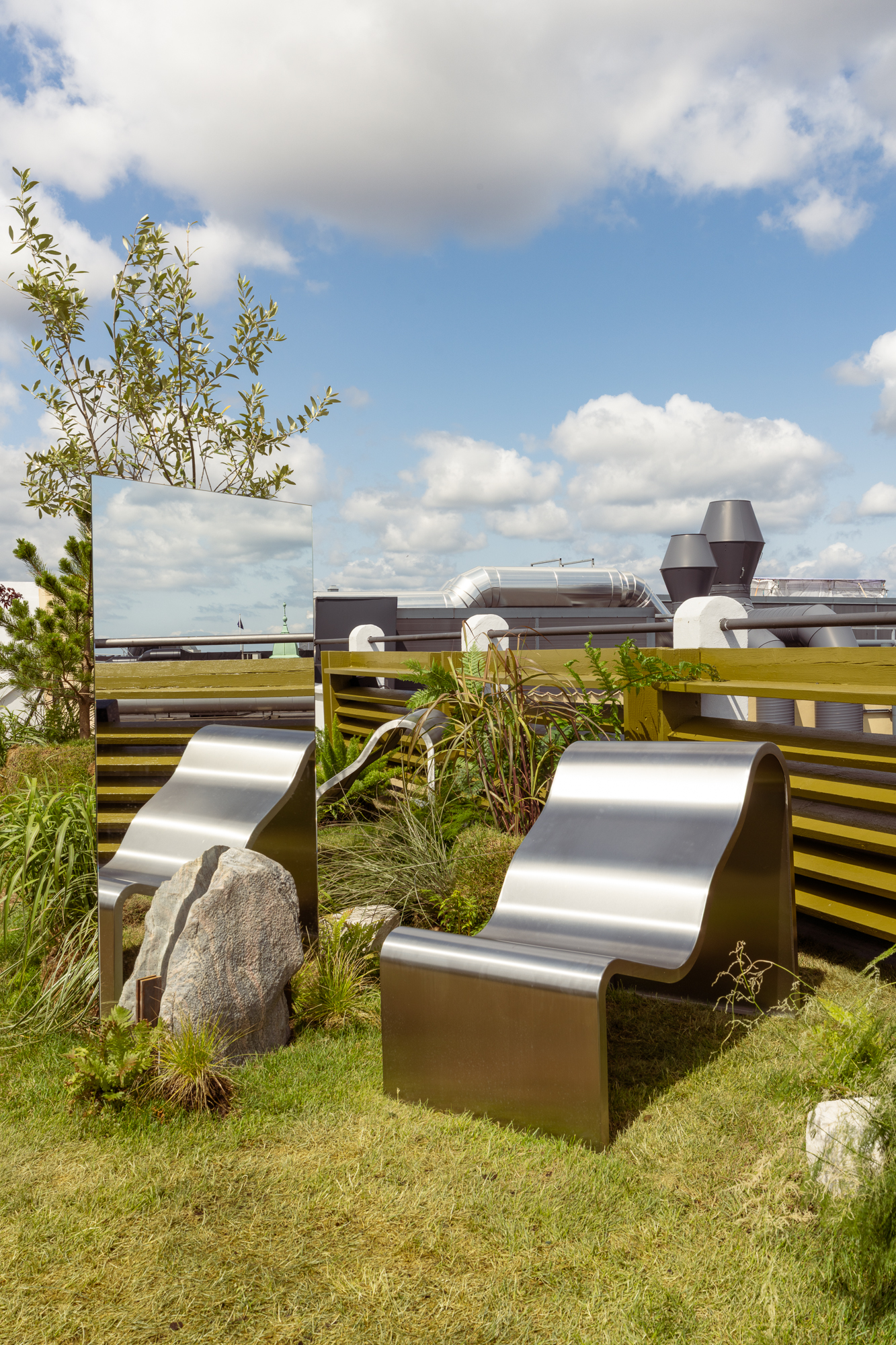 An image of the Dream View Bench placed on a rooftop surrounded by lush green plants and grass, creating a serene and calming atmosphere.