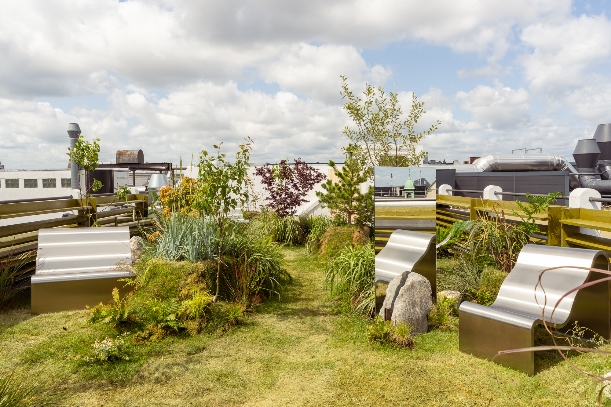 An image of the Dream View Bench placed on a rooftop surrounded by lush green plants and grass, creating a serene and calming atmosphere.