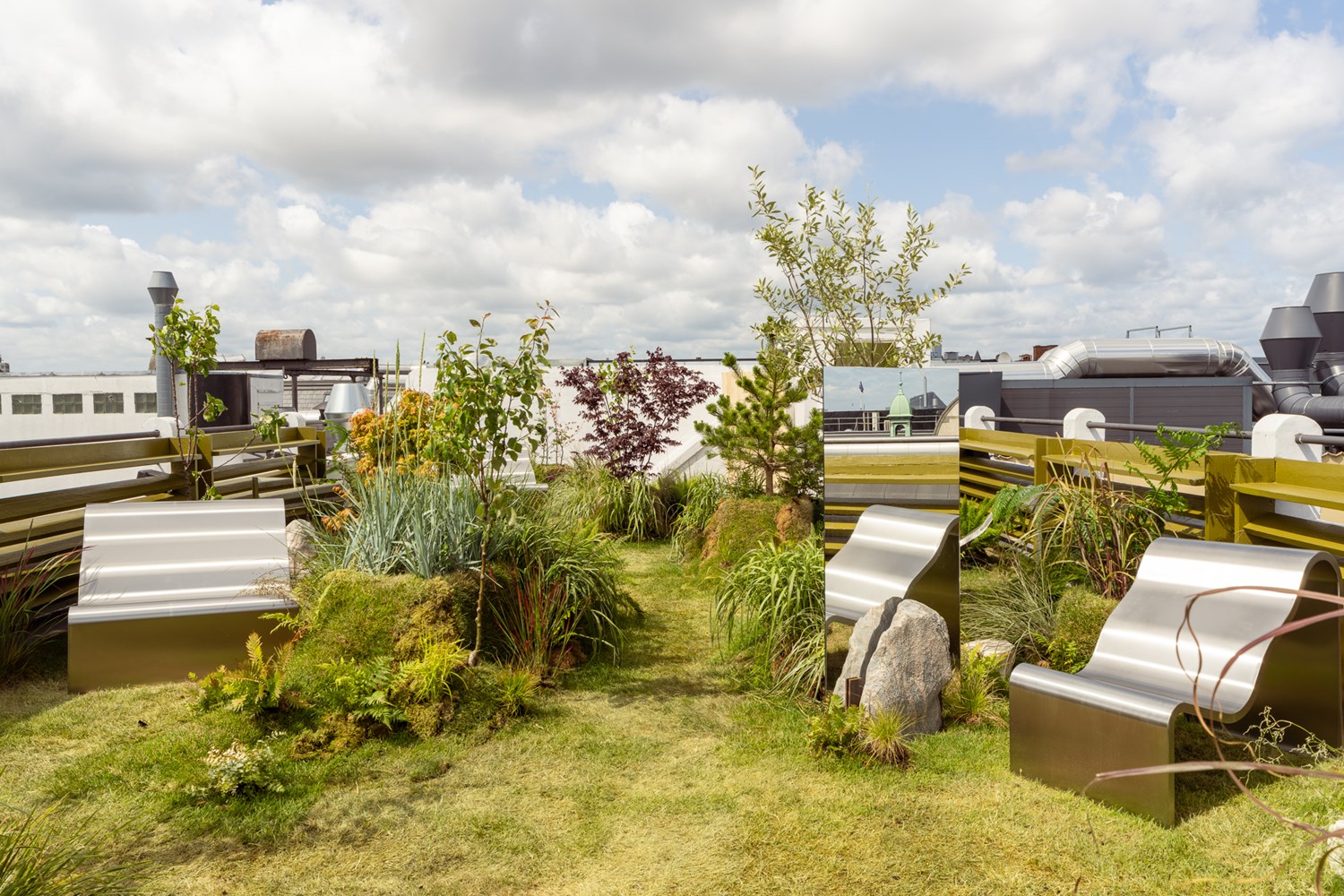 An image of the Dream View Bench placed on a rooftop surrounded by lush green plants and grass, creating a serene and calming atmosphere. An image of the Dream View Bench placed on a rooftop surrounded by lush green plants and grass, creating a serene and calming atmosphere.