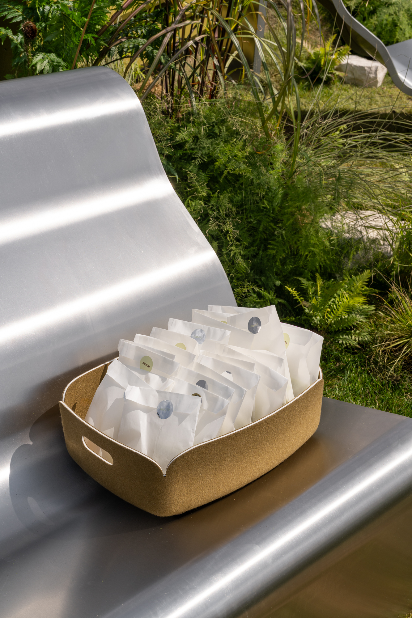 A green Restore basket with paper bags placed on a Dream View Bench.