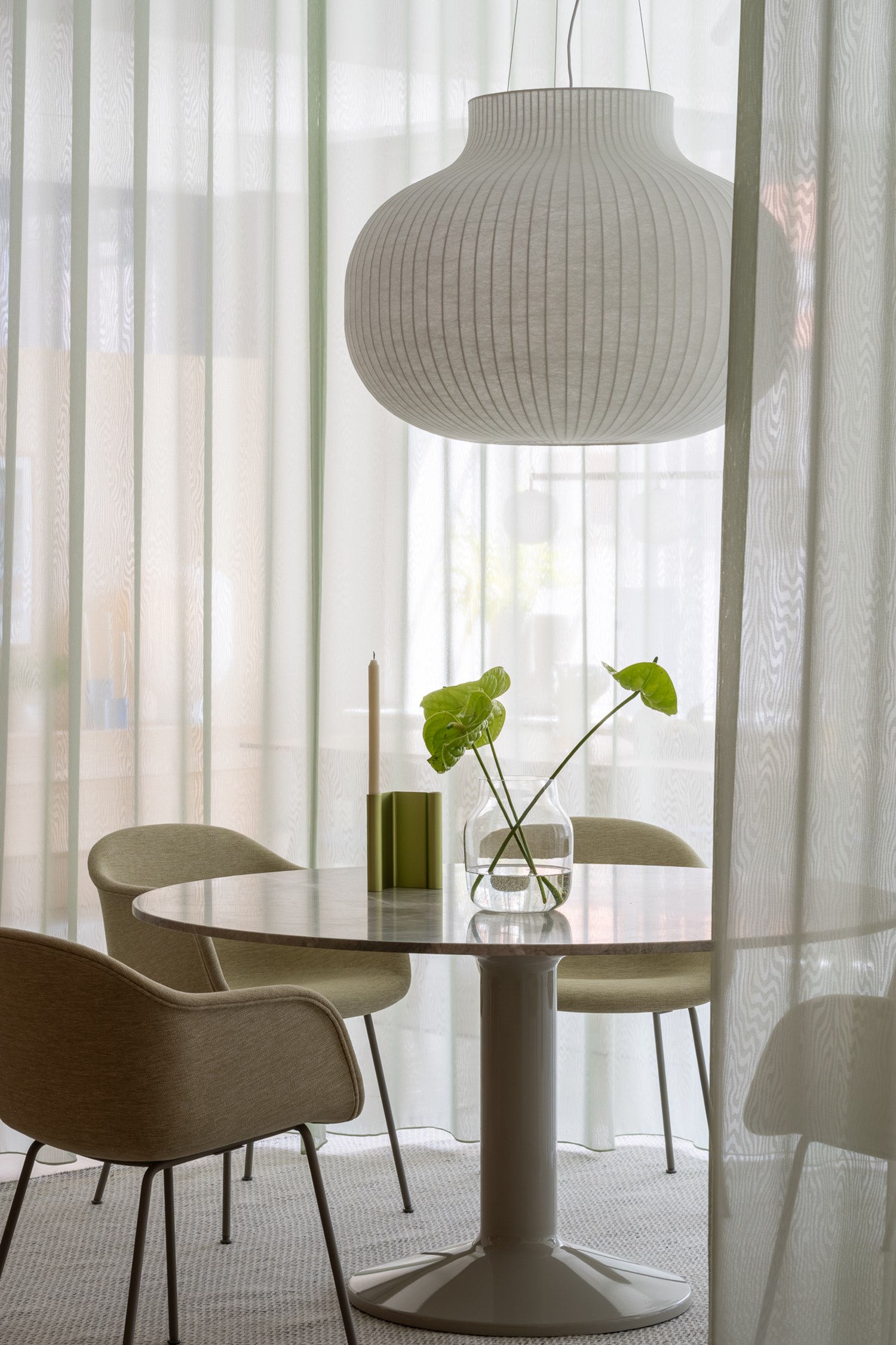 The Midst table in marble is placed in a white room with modern curtains. Soft green chairs surround the table, while a pendant lamp hangs above, adding a cozy touch to the space. The Midst table in marble is placed in a white room with modern curtains. Soft green chairs surround the table, while a pendant lamp hangs above, adding a cozy touch to the space.