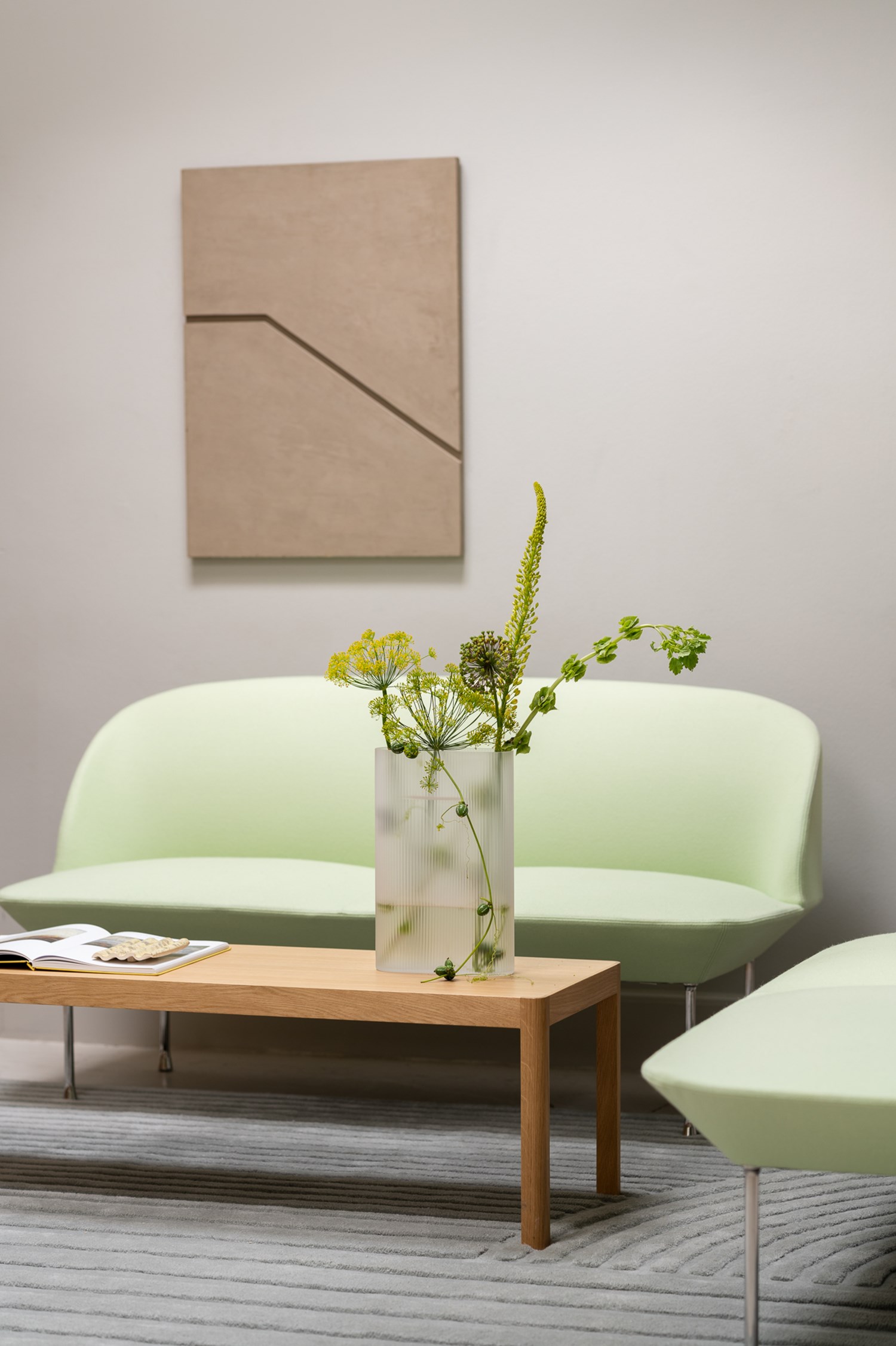 The Oslo Sofa in light green is placed behind a minimalist wooden coffee table. An artistic, minimalistic vase with green flowers sits on the table, adding a cozy and inviting touch to the room. The Oslo Sofa in light green is placed behind a minimalist wooden coffee table. An artistic, minimalistic vase with green flowers sits on the table, adding a cozy and inviting touch to the room.