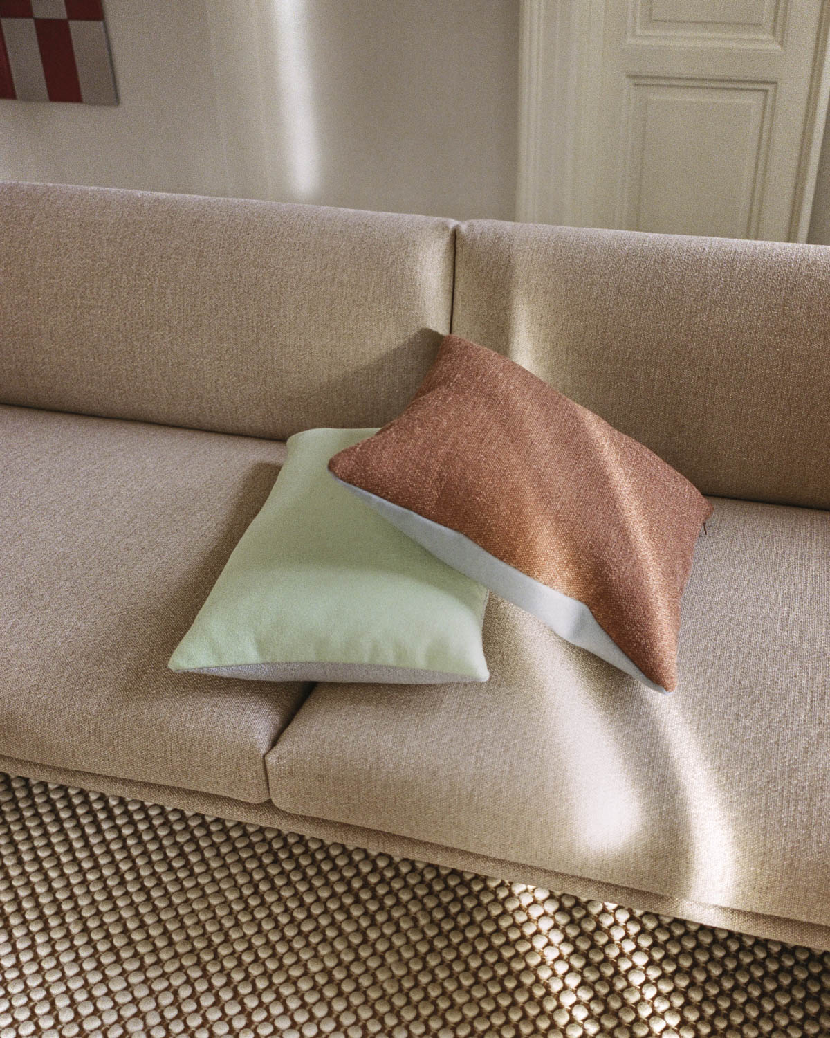 Close-up view of a beige textured sofa adorned with two pillows in soft green and brown.