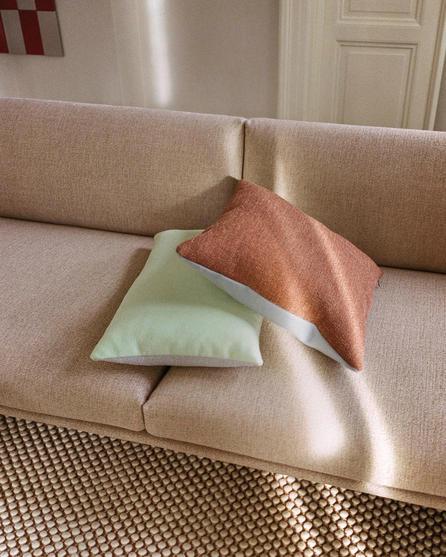 Close-up view of a beige textured sofa adorned with two pillows in soft green and brown. Close-up view of a beige textured sofa adorned with two pillows in soft green and brown.