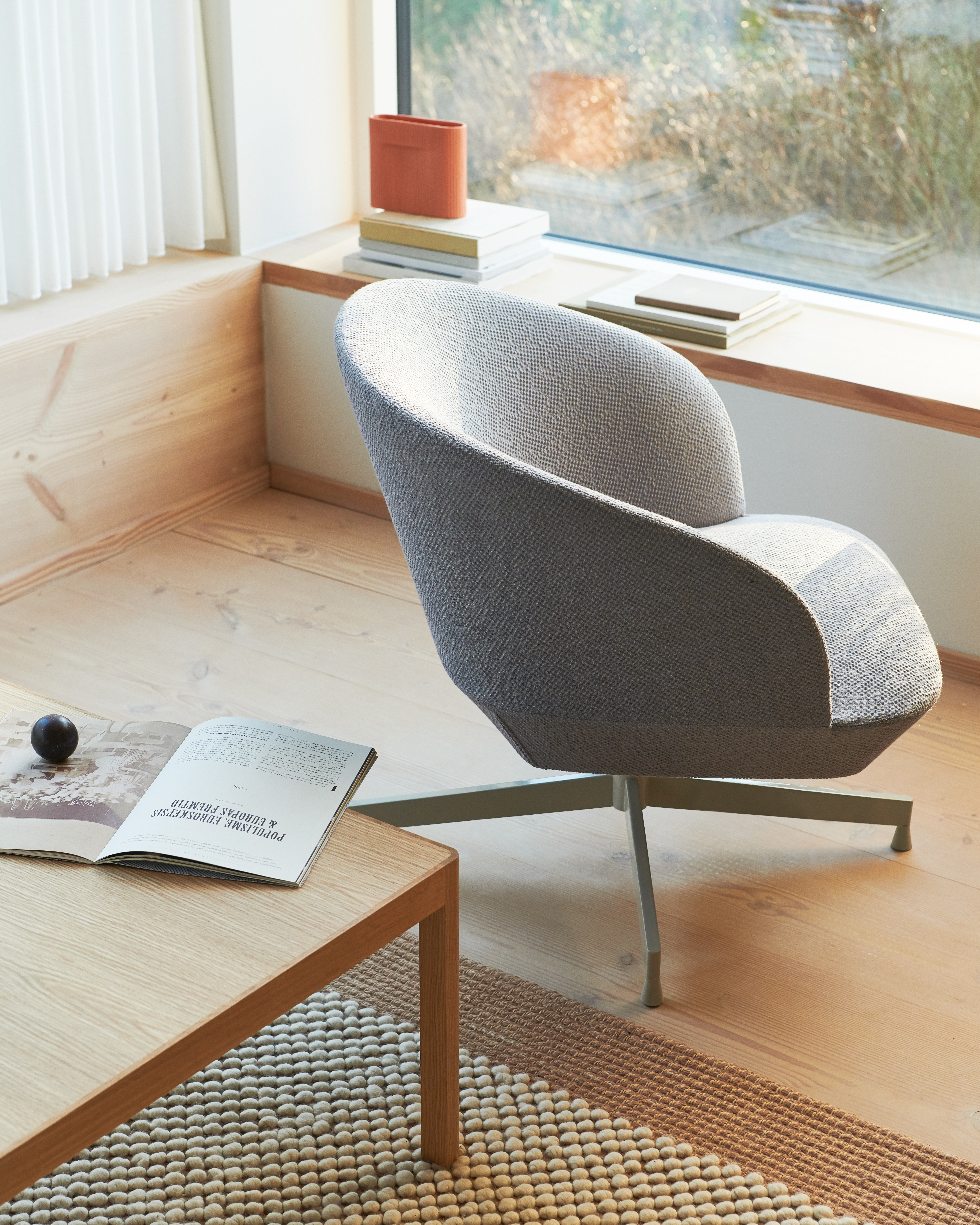 A reading nook showcasing a textured gray armchair by a window, paired with a wooden coffee table and a neutral rug,.