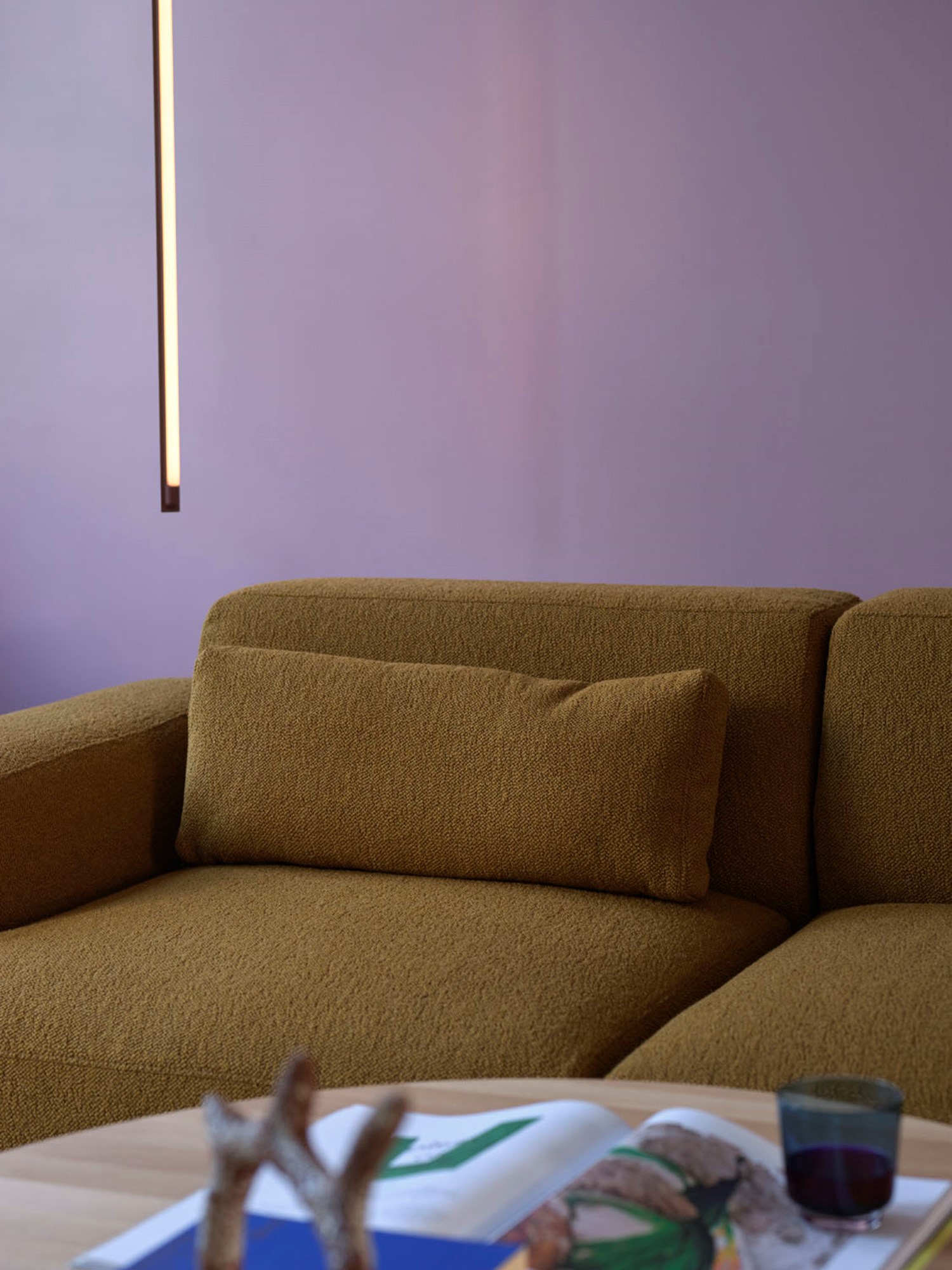 Modern brown green sofa in a minimalist living room with purple walls and a sleek, vertical light fixture, conveying a cozy yet contemporary ambiance. Modern brown green sofa in a minimalist living room with purple walls and a sleek, vertical light fixture, conveying a cozy yet contemporary ambiance.