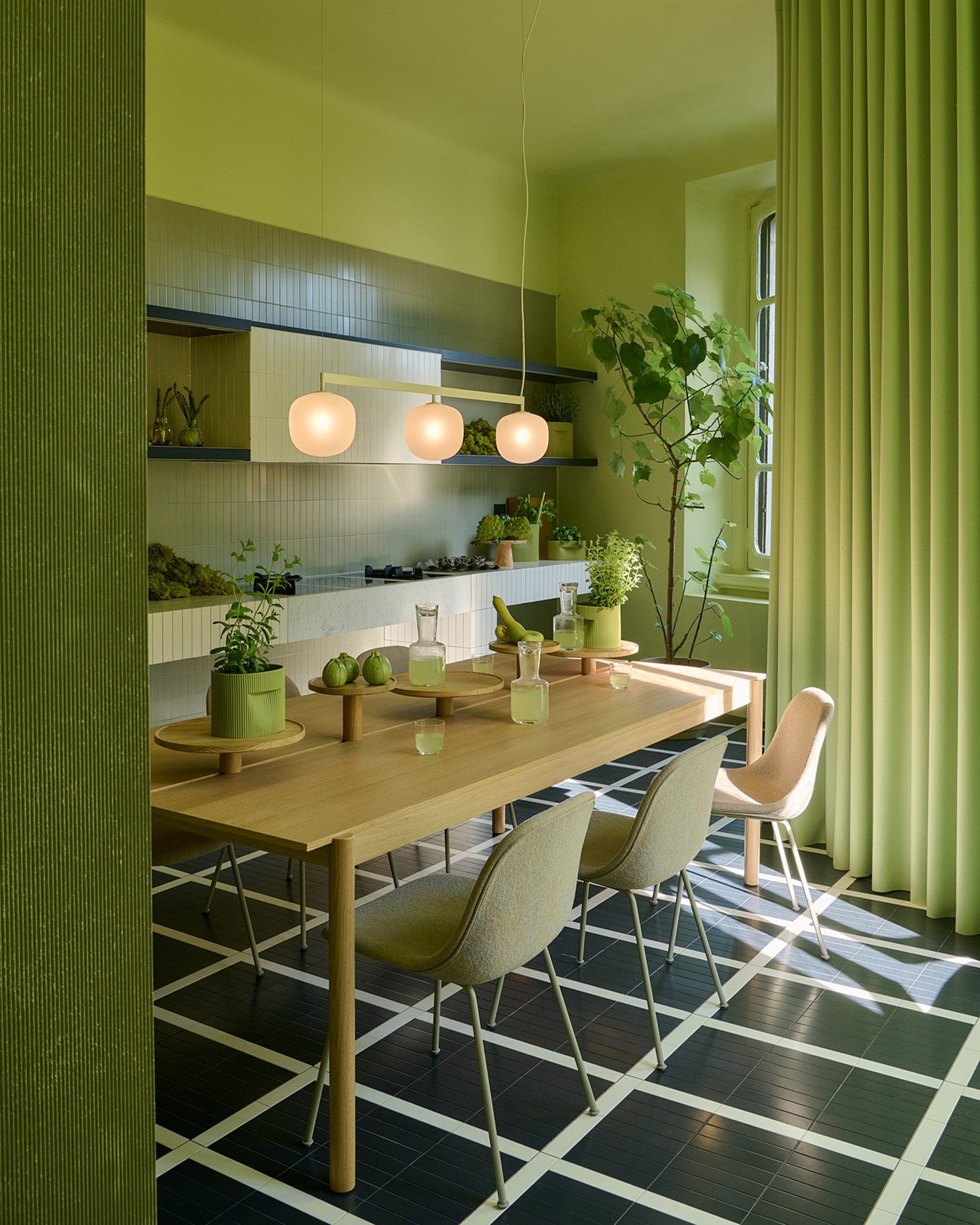 Image of Muuto's Milan Apartment. A ligtht green room with a wooden dining table and chairs. A pendal is placed above the table and green vases are matching the light green surroundings.  Image of Muuto's Milan Apartment. A ligtht green room with a wooden dining table and chairs. A pendal is placed above the table and green vases are matching the light green surroundings.