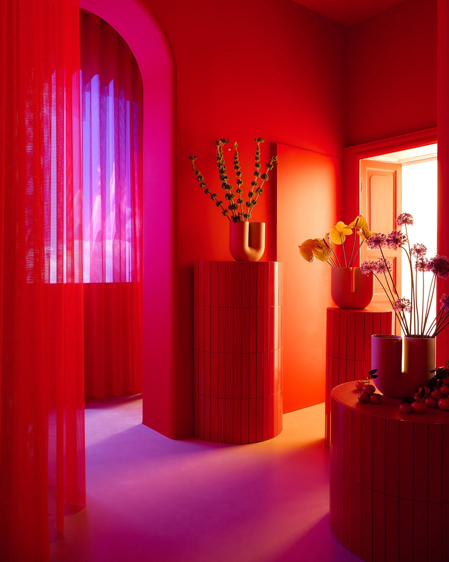 A red room with red curtains in Muuto's Milan apartment for Milan Design Week 2025. Sculptural vases with flowers are placed arround the room on stone pedistals in different heights.  A red room with red curtains in Muuto's Milan apartment for Milan Design Week 2025. Sculptural vases with flowers are placed arround the room on stone pedistals in different heights.