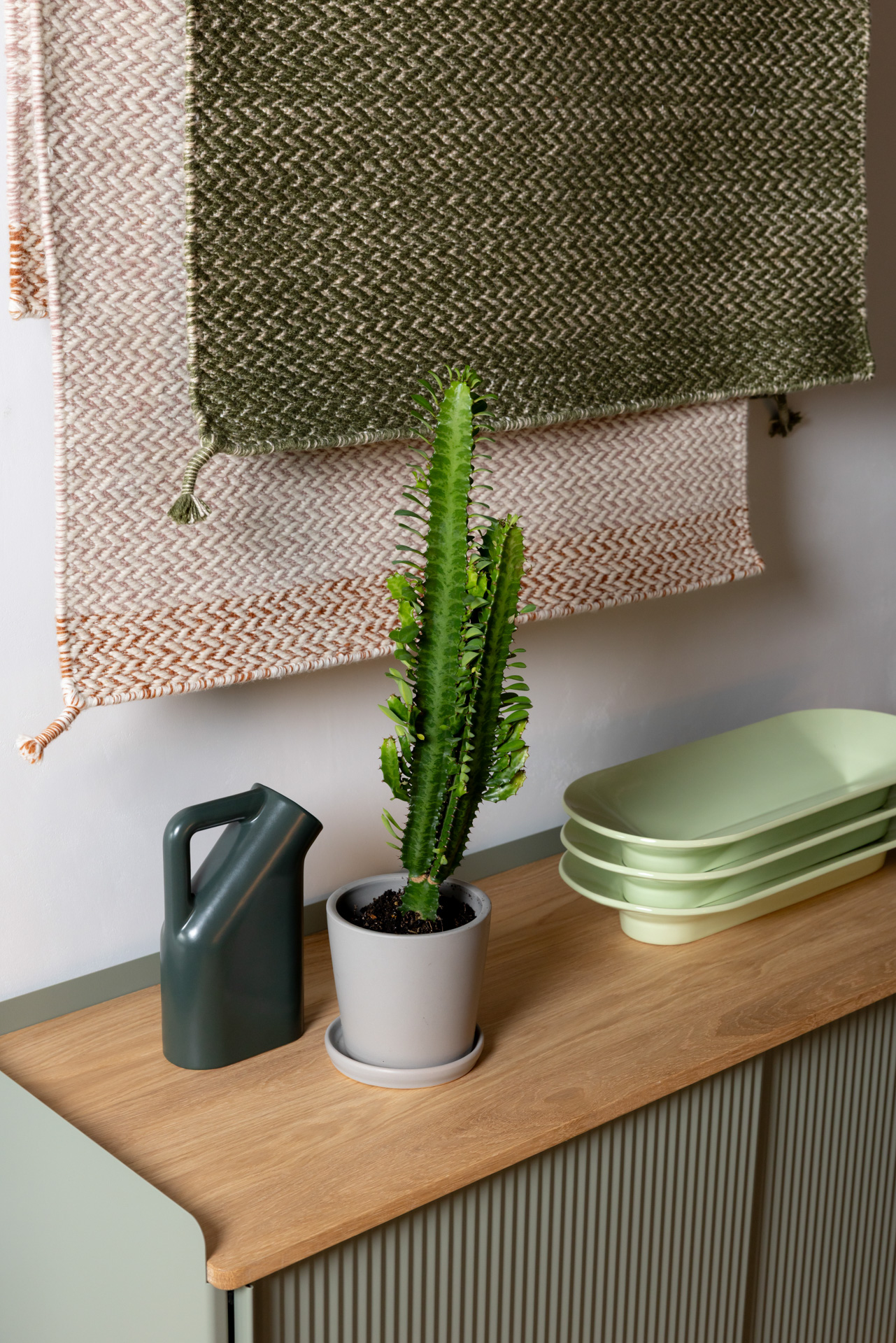The Enfold Side Table is placed against a grey wall, styled with a green plant and a light green bowl on top.