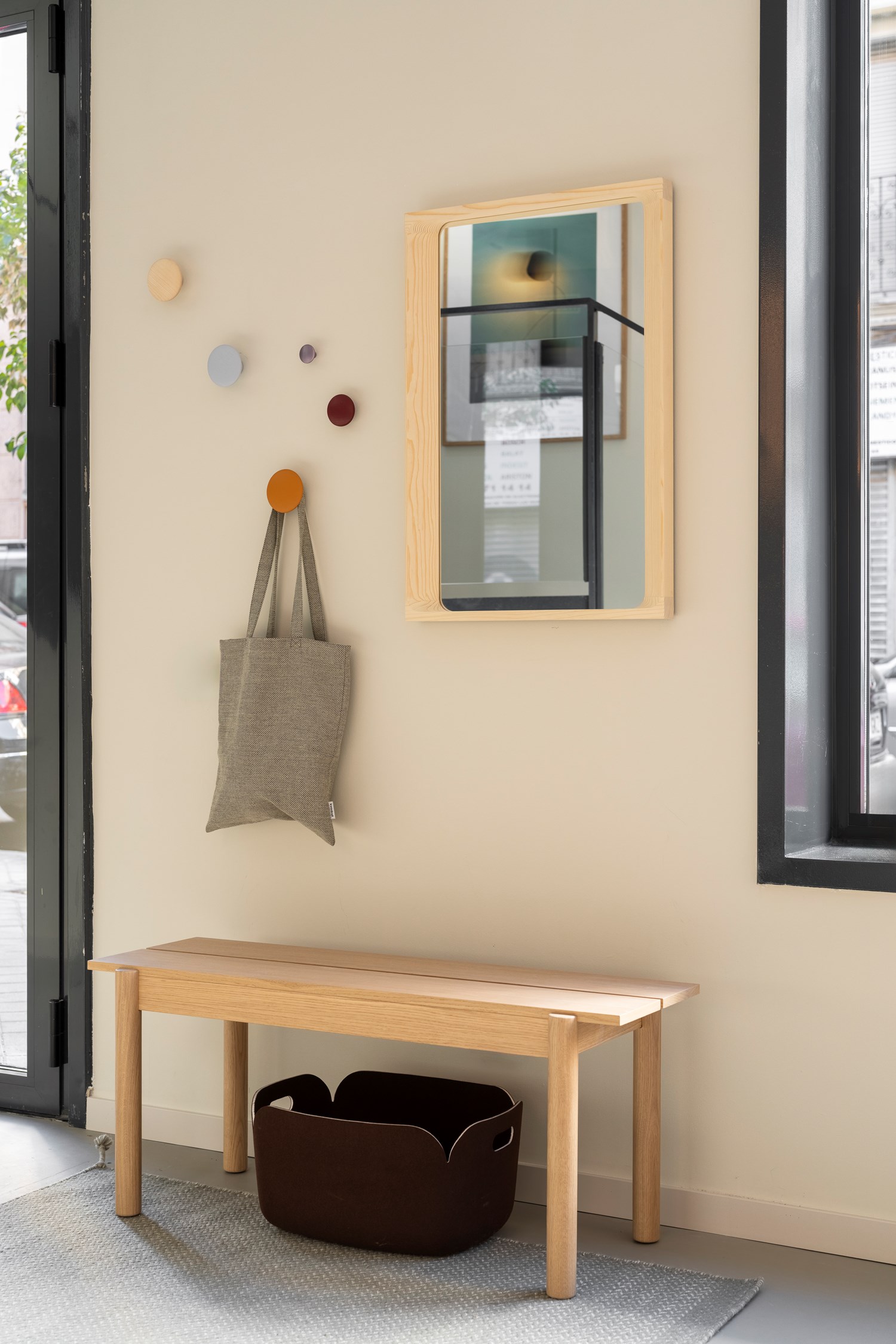 Entryway scene from the Muuto showroom in Madrid featuring the Linear Wood Bench in oak, styled with arced mirror, colorful Dots hooks  and a dark brown restore basket for a functional and welcoming setting. Entryway scene from the Muuto showroom in Madrid featuring the Linear Wood Bench in oak, styled with arced mirror, colorful Dots hooks  and a dark brown restore basket for a functional and welcoming setting.